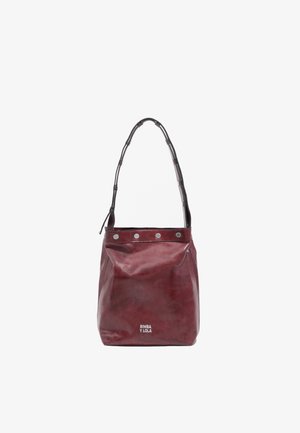 Červená kožená vedierková taška s okrúhlym tvarom, širokým ramenným popruhom, striebornými cvočkami pozdĺž horného okraja a s logom značky na prednej strane.
