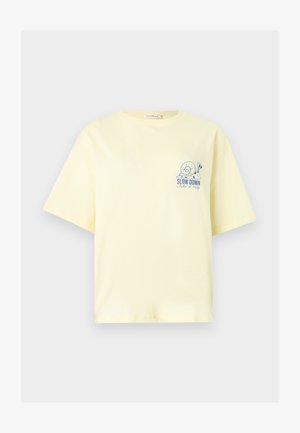 Απαλό κίτρινο μπλουζάκι με κοντά μανίκια, με ένα μπλε σαλιγκάρι και το κείμενο «SLOW DOWN Take it easy» στην αριστερή πλευρά του στήθους.