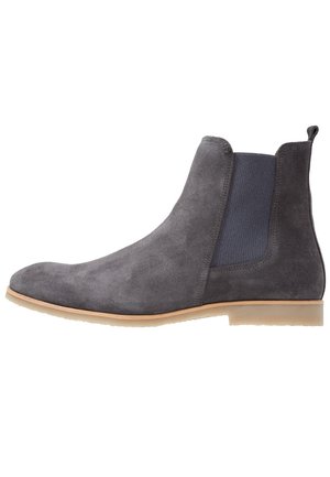 Bottine Chelsea en daim gris avec un panneau latéral élastique et une semelle en caoutchouc beige, vue de côté extérieur sur fond blanc.