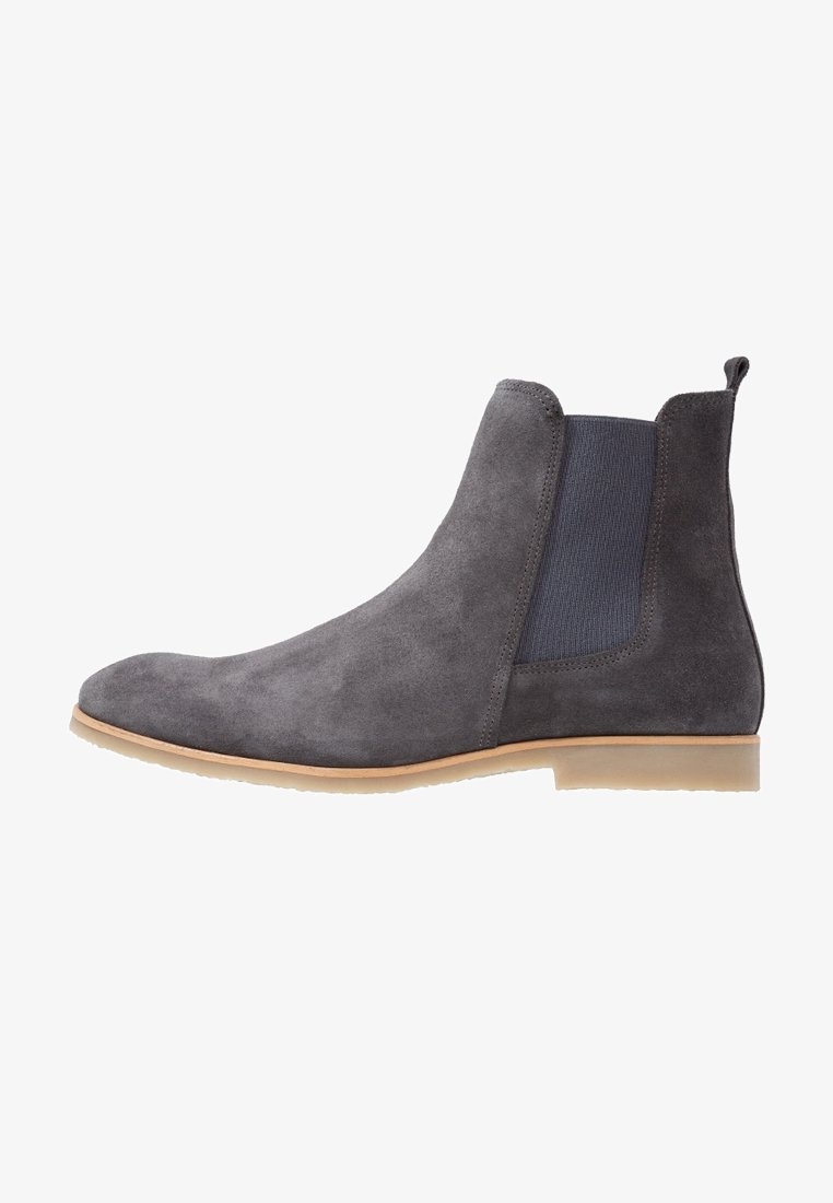 Bottine Chelsea en daim gris avec un panneau latéral élastique et une semelle en caoutchouc beige, vue de côté extérieur sur fond blanc.