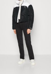 Černá péřová bunda s bílými rameny, se zipem vpředu a logem Calvin Klein. Kombinováno s černými džíny a bílými teniskami.