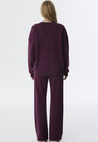 Übergroßer Pullover und weit geschnittene Hose aus tiefviolettem Stoff. Weiche Textur mit gerippten Bündchen, lässiger Schnitt und ohne sichtbare Hardware oder Muster.