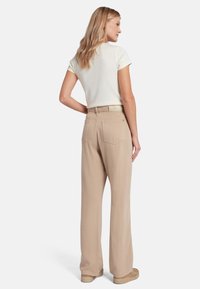 Beige wijde broek van zacht materiaal met een gladde textuur. Voorzien van twee achterzakken en een subtiele logo op de tailleband.