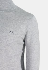 Maglione grigio a collo alto in un morbido tessuto a maglia, con un sottile logo ricamato in blu navy sul petto. Design aderente con maniche lunghe.