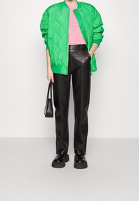 Persoon in een felgroene gewatteerde jas, roze top, zwarte leren broek, zwarte chunky laarzen en met een kleine zwarte handtas.