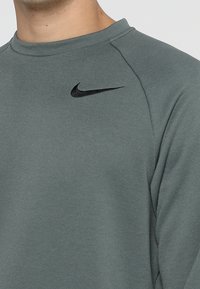 Bluza Nike w ciemnozielonym kolorze, wykonana z miękkiego materiału, z okrągłym dekoltem i raglanowymi rękawami; posiada czarne logo na piersi.