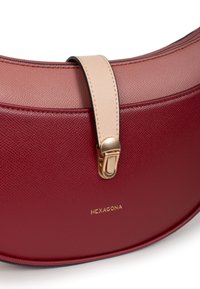 Borsa a tracolla in pelle rossa e rosa con forma curva, dotata di una tracolla beige e accessori in oro. Logo "HEXAGONA" impresso sul fronte.