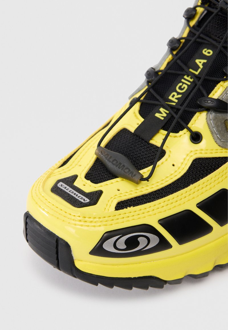 Baskets jaunes avec une tige en maille, des accents noirs et un motif de semelle distinctif. Comprend des détails texturés et des éléments de marque.