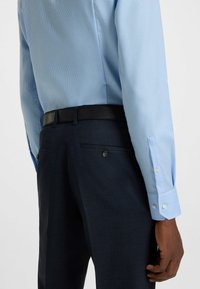 Vaaleansininen ruudullinen paita, jossa on valkoiset napit, yhdistetty tummansinisiin housuihin. Mukana musta nahkavyö. Huomattavissa tekstuuri kankaassa.