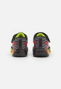 Sorte sneakers med reflekterende grå striber, neongrønne detaljer og røde elementer. Har en velcrostrop og en struktureret sort ydersål.