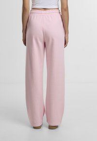 Lyserøde, brede sweatpants med elastisk talje. Blød stofftekstur, minimalistisk design og afslappet pasform.