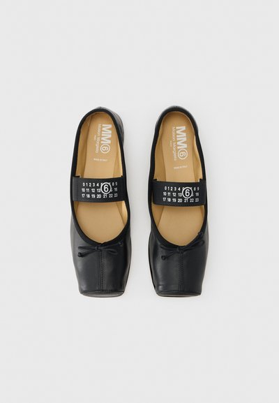 Μαύρα μπαλαρίνια από δέρμα με στρογγυλεμένη μύτη, ελαστική ταινία και διακοσμητικό φιόγκο. Το εσωτερικό διαθέτει ταμπά πάτο με λογότυπο.