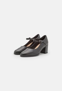 Chaussures Mary Jane en cuir noir avec un bout rond, une sangle ajustable et un talon carré. Texture lisse avec un design minimaliste.