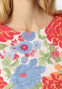 Floral-patterned fabric featuring large blossoms in blue, red, and green on a cream background with a round neckline. Smooth texture.
