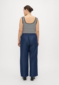 Top sem mangas listrado em preto e branco, combinado com calças largas de cintura alta em azul escuro. Design minimalista com faixa elástica na cintura.