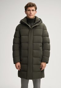 Cappotto trapuntato verde oliva con collettore alto, design trapuntato e tasche laterali. Presenta una chiusura con zip e un cappuccio, che arriva fino a metà coscia.