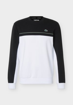 Langermet genser med rund hals, svart overdel og ermer, hvit kropp, tynn stripe over brystet og liten grønn krokodillelogo.