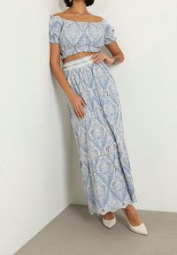 Lys blå to-delt outfit bestående af en cropped, flæse-top og en lang nederdel med intrikate blonder og bølgede kanter. Hvide hæle.