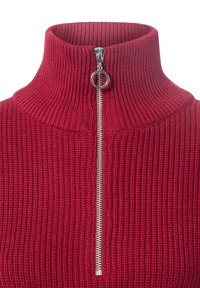 Czerwony sweter prążkowany z wysokim kołnierzem i srebrnym zamkiem błyskawicznym. Posiada strukturalny wzór oraz okrągły uchwyt zamka.