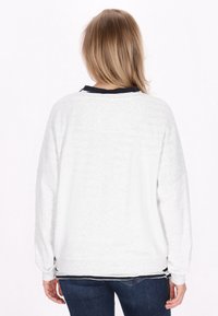 Felpa oversize grigio chiaro con maniche lunghe, polsini a costine e scollatura nera. Tessuto testurizzato con una vestibilità comoda, indossata con jeans scuri.