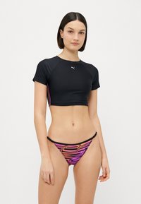 Μαύρο κοντό αθλητικό τοπ με κοντά μανίκια και ροζ λεπτομέρεια, συνδυασμένο με χαμηλής μέσης μπικίνι που διαθέτει έντονο μοτίβο σε μαύρο, ροζ και πορτοκαλί.