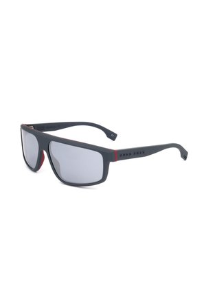 Occhiali da sole sportivi con montatura rettangolare nera, lenti grigie e dettagli rossi sulle aste e all'interno delle aste.