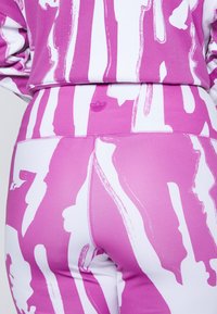 Sada fitted sportovního oblečení v růžové a bílé barvě s odvážným štětcovým vzorem. Měkká, elastická tkanina s logem na pásku.