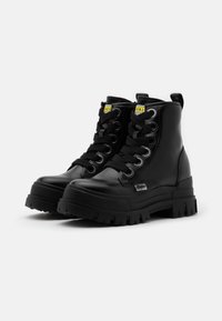 Bottes de combat noires avec une finition brillante, bout rond, semelle en caoutchouc épaisse et œillets métalliques. Comprend des lacets et une languette à l'arrière.