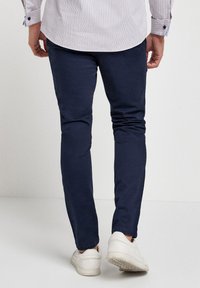 Mornarsko modri slim-fit hlače iz mehkega blaga, z gladko teksturo, v kombinaciji z belimi supergami in črtasto srajco.