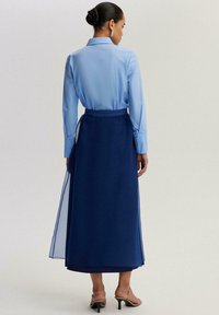 Hele sinine pluus kraega, kombineeritud pika tumesinise seeliku ja läbipaistvate kangakihtidega. Kõrge kontsaga sandaalid rõhutavad komplekti.