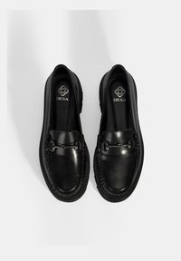 Zwarte leren loafers met een ronde neus, gestikte details en een kleine metalen accent aan de voorkant. Slipvaste rubberen zool voor grip.