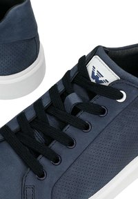 Námořnické kožené tenisky s perforovanou panelem, černými tkaničkami a bílými akcenty. Mají značkovou etiketu na boku a bílou gumovou podrážku.