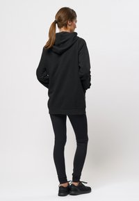 Zwarte hoodie met een ruime pasvorm, capuchon met trekkoord en lange mouwen, gecombineerd met zwarte leggings en zwarte sportschoenen.