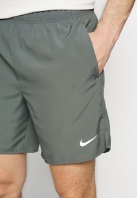 Grå sportshorts med elastisk midja, sidfickor och en vit Nike-logga på nedre vänstra fållen. Slät, lättviktsmaterial.
