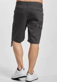 Graue Cargo-Shorts mit Seitentaschen, elastischem Bund und Kordelzügen. Kombiniert mit weißen Turnschuhen mit schwarzen Akzenten.
