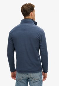 Pile blu navy con collo alto e maniche lunghe. Presenta una texture morbida e un dettaglio di cucitura sottile lungo la parte superiore della schiena.