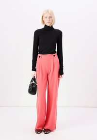 Črno turtleneck majico, roza široke hlače s tremi sprednjimi gumbi, nosi majhno črno torbico in obuje črne čevlje z leopardjim vzorcem.