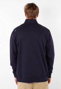 Sweat-shirt marine à col haut et manches longues ; texture douce ; présente un logo sur l'épaule gauche et des poignets et un ourlet côtelés.