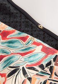 Gros plan de deux masques en tissu, l'un noir avec une texture en dentelle, l'autre avec un motif abstrait coloré de feuilles, tous deux avec de petites breloques de logo circulaires en or.