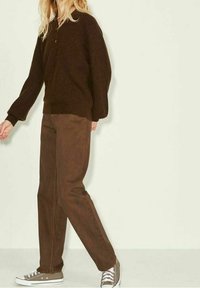 Brauner Strickpullover mit hohem Kragen und weiter Passform, kombiniert mit braunen, gerade geschnittenen Hosen und grauen Turnschuhen. Einfaches und lässiges Outfit.