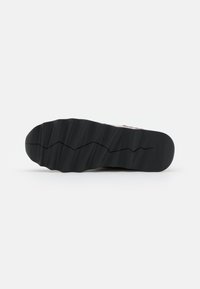 Sole di sneaker nera in gomma con un motivo di battistrada a zigzag e linee verticali. Presenta il logo del marchio in rilievo vicino al tallone.