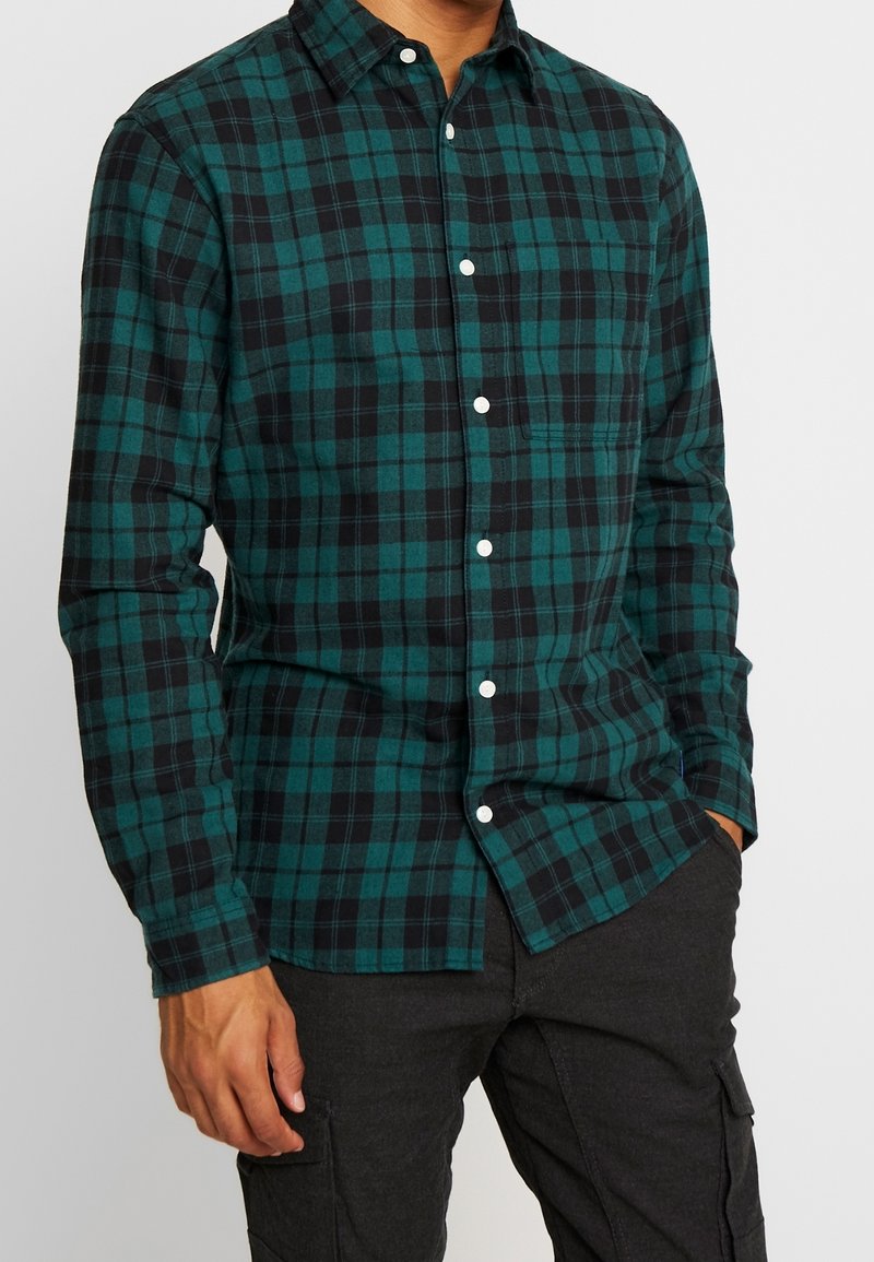 Karierter Flanellhemd mit grün-schwarzem Farbschema, Knopfverschluss, langen Ärmeln und einer Brusttasche.