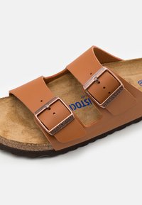 Tan leather sandal with two adjustable straps, copper-tone buckles, cork footbed, and dark rubber sole. Textured upper and soft interior.