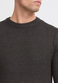 Suéter de punto gris oscuro con cuello redondo, que presenta un patrón texturizado y puños acanalados. Diseñado para un ajuste ceñido.