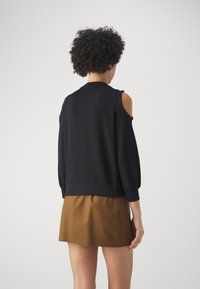 Sudadera negra con cortes en los hombros, puños acanalados y dobladillo. Combinada con una falda marrón en forma de A, con una textura suave y un diseño sencillo.
