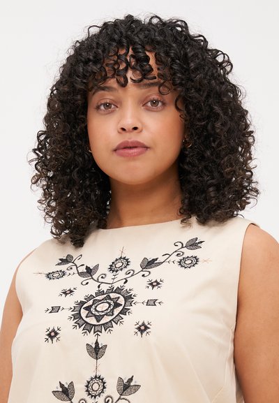 Débardeur beige sans manches présentant une broderie noire complexe avec des motifs floraux et géométriques, une texture de tissu lisse et une coupe décontractée.