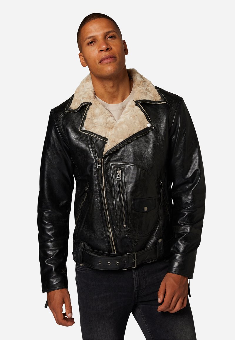 Svart läderjacka med krage i fuskpäls, med flera dragkedjefickor, bälte i midjan och texturerad yta. Klassisk motorcykeldesign.