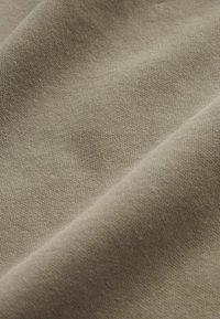 Helles braunes Baumwollgewebe mit glatter Textur, das feine, eng gewobene Fäden und subtile Farb- und Tiefevariationen aufweist.