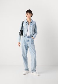 Lys blå denimjakke over en hvit t-skjorte, parret med løstsittende lys blå jeans og hvite sneakers. En svart håndveske henger fra venstre skulder.