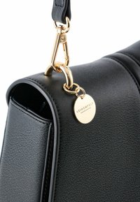 Angolo di borsa in pelle nera con chiusura in metallo dorato, tracolla corta e medaglione rotondo in oro inciso con la scritta "SEIDENFELT MANUFAKTUR."